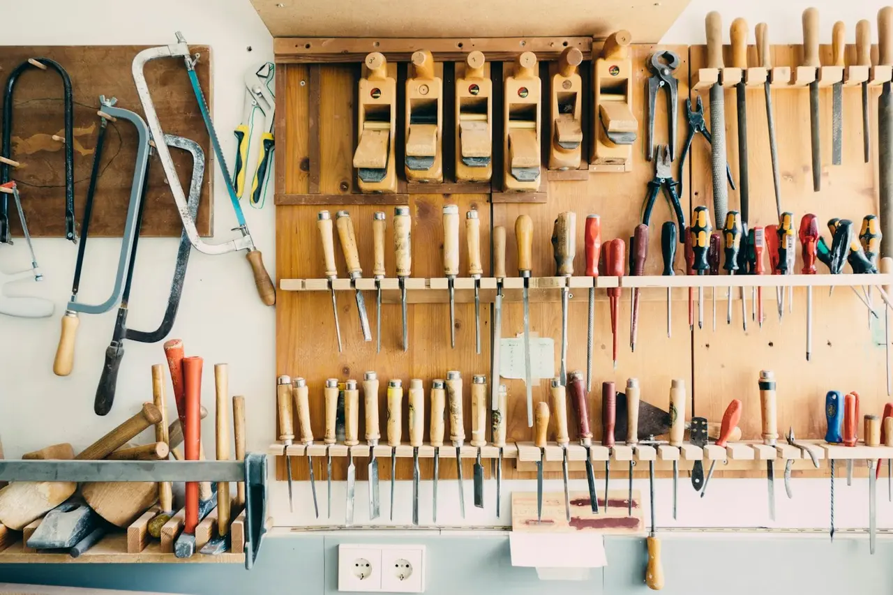Mur d'atelier garni d'outils à main : ciseaux à bois, rabots, scies, tournevis et limes.